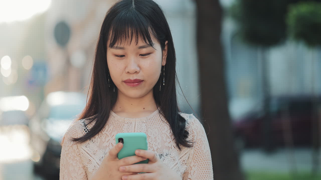 An Asian woman holding a phone outdoors