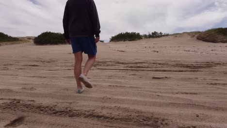 hombre con pantalones cortos caminando por la playa de arena y saliendo durante un día nublado en argentina, primer plano de la pista