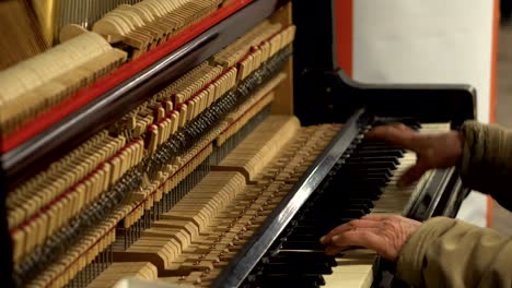 hands of old man in subway underground playing piano with opened mechanism og strings and hammers