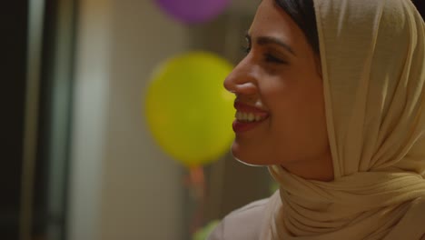 close up of woman giving female friend birthday present at home with party balloons in background