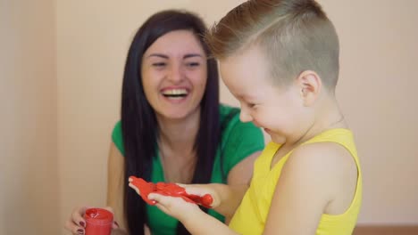 Happy-mother-and-her-little-son-are-painting-using-red-color-with-hands-that-are-dirty