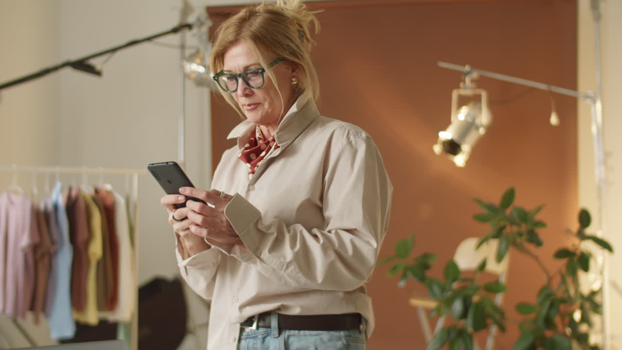 Donna matura che usa lo smartphone al lavoro in studio fotografico