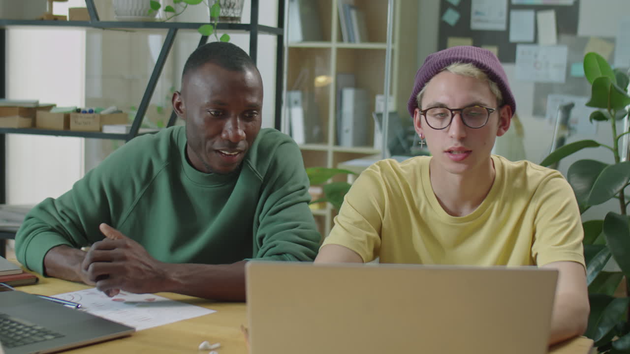 Multiethnic Gen Z Colleagues Using Laptop and Speaking in Office