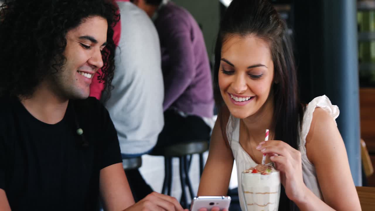 pareja usando el teléfono móvil mientras toman un batido en un pub