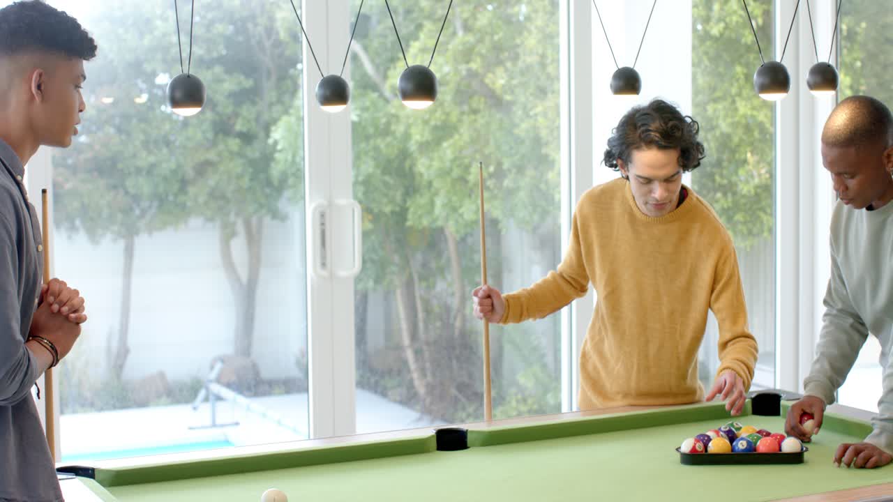 After exchanging cues, Diverse male friends in home game room racking billiard balls to start match