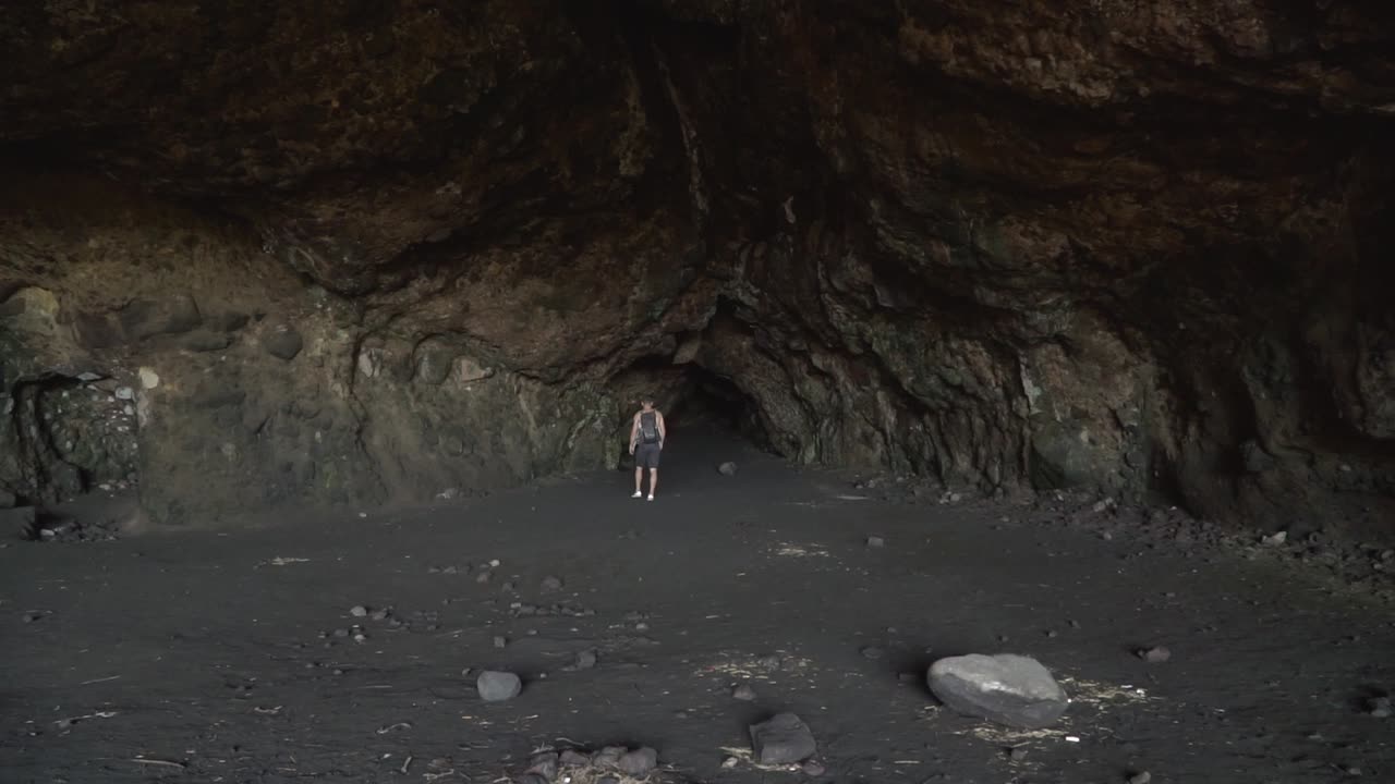 slowmo - joven caucásico caminando hacia una cueva de lava oscura en nueva zelanda