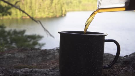 Vertiendo-Café-Recién-Hecho-En-Una-Taza-En-El-Desierto-Con-Vistas-Espectaculares-A-Un-Bosque-Y-Un-Río-Desde-Una-Pendiente