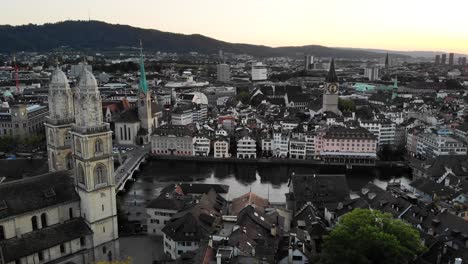 Flyover-alongside-Limmat-river-in-Zurich,-Switzerland-with-view-of-Grossmünster-from-behind-and-rest-of-downtown