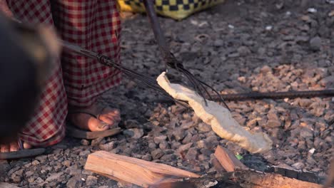 close shot of flat bread being cooked over open flames with two long sticks with prongs at the end of them to flip the bread