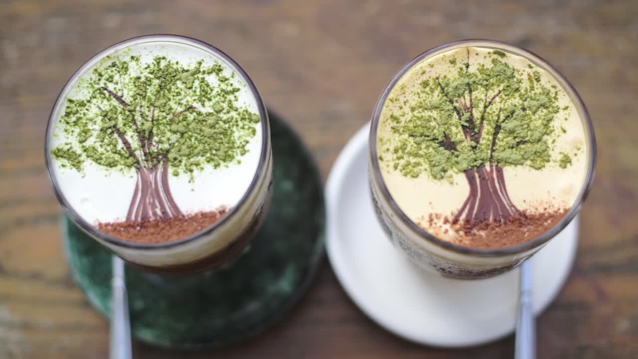 Tazze da caffè con guarnizioni decorative. Vista dall'alto di bevande al caffè su un tavolo di legno. Scena che mostra due tazze da caffè con spolverata di matcha e decorazioni a forma di tronco di cacao su schiuma testurizzata.