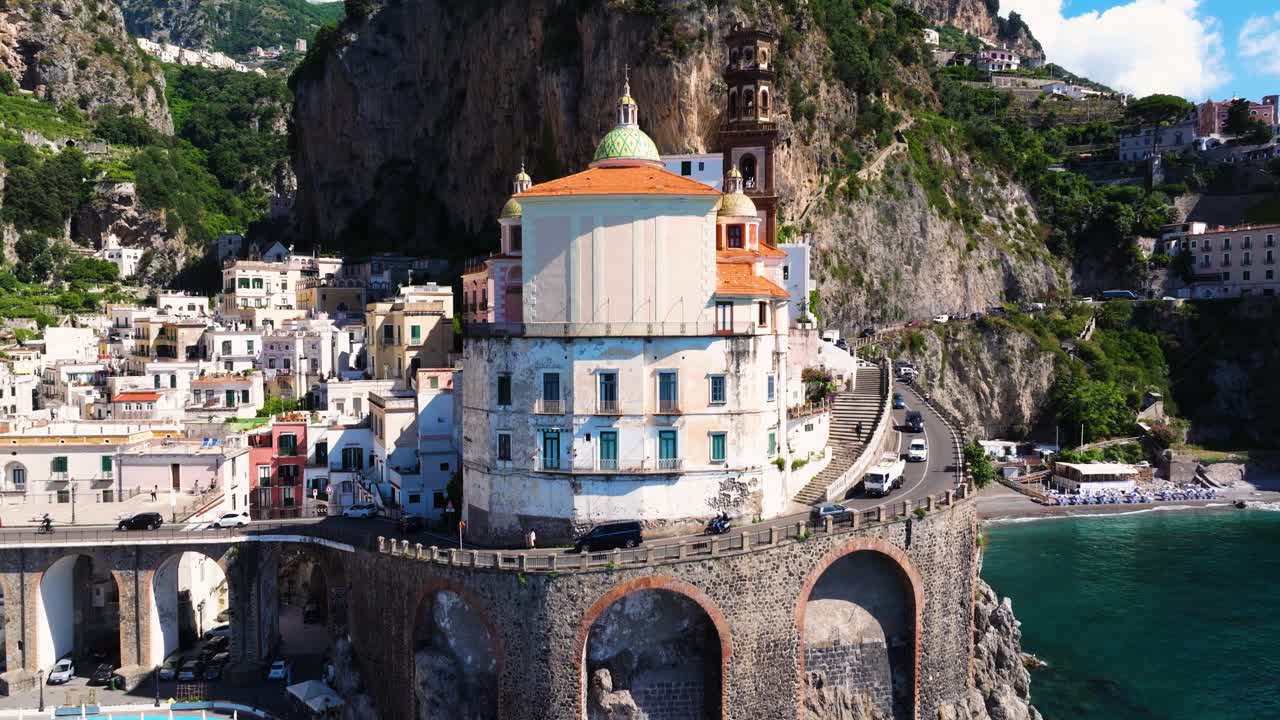 Ripresa aerea con movimento verticale sopra Atrani mentre le auto guidano lungo la Costiera Amalfitana, Italia