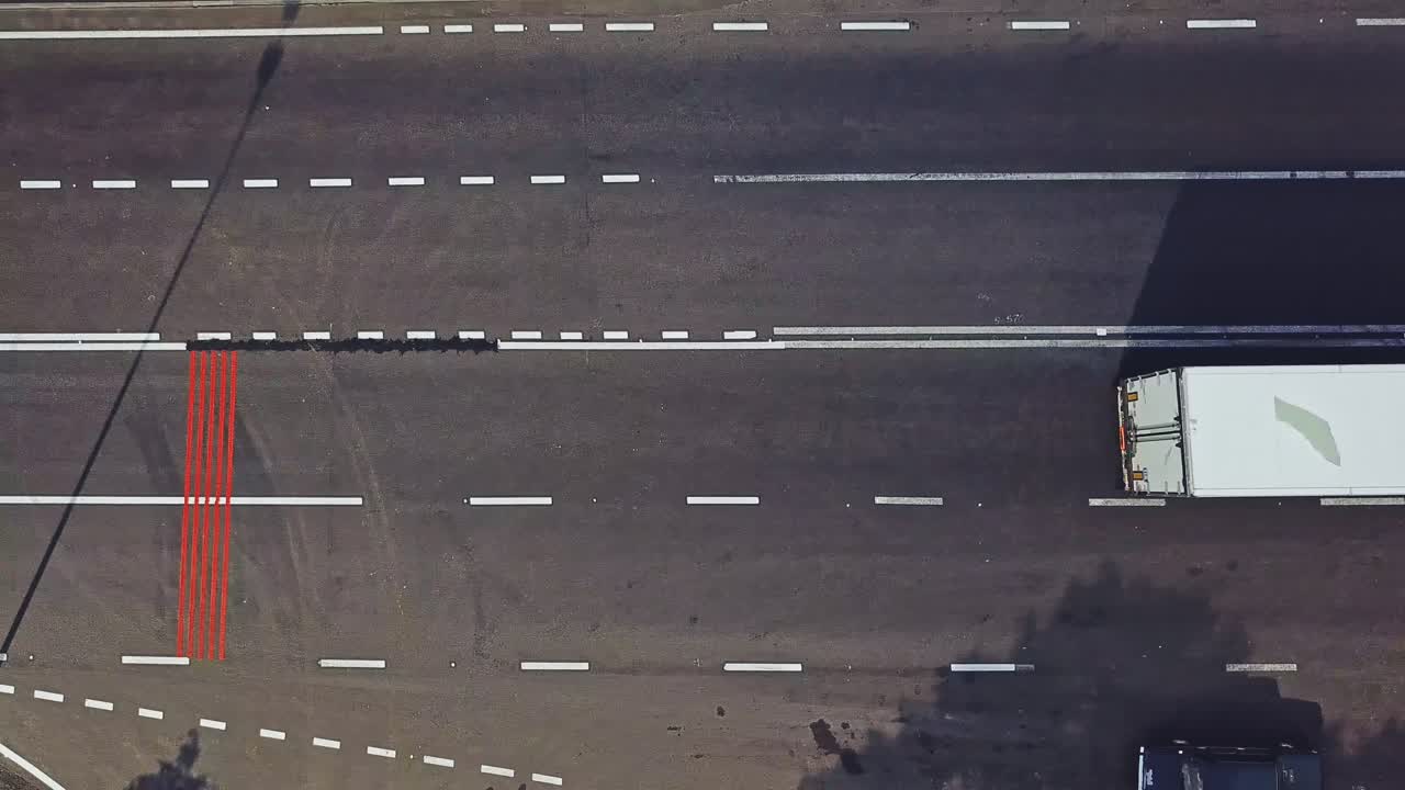 Few long vertical red stripes painted on one side of the road surface and cars passing. Aerial view of wide asphalt road divided into two opposite sides for cars. Camera moves right