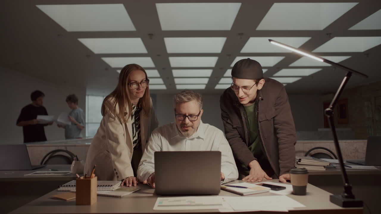 Senior Businessman Discussing Data on Laptop with Coworkers in Office