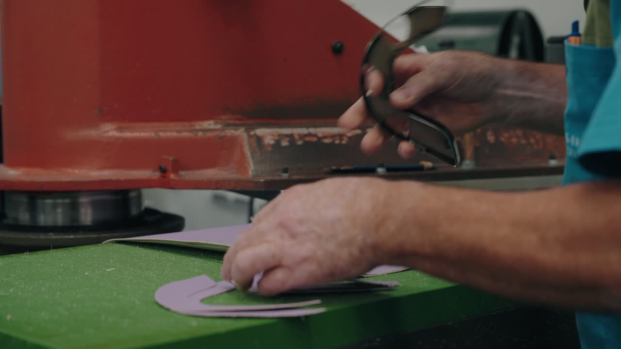 Primer plano de un trabajador usando una máquina para cortar patrones de zapatos de cuero