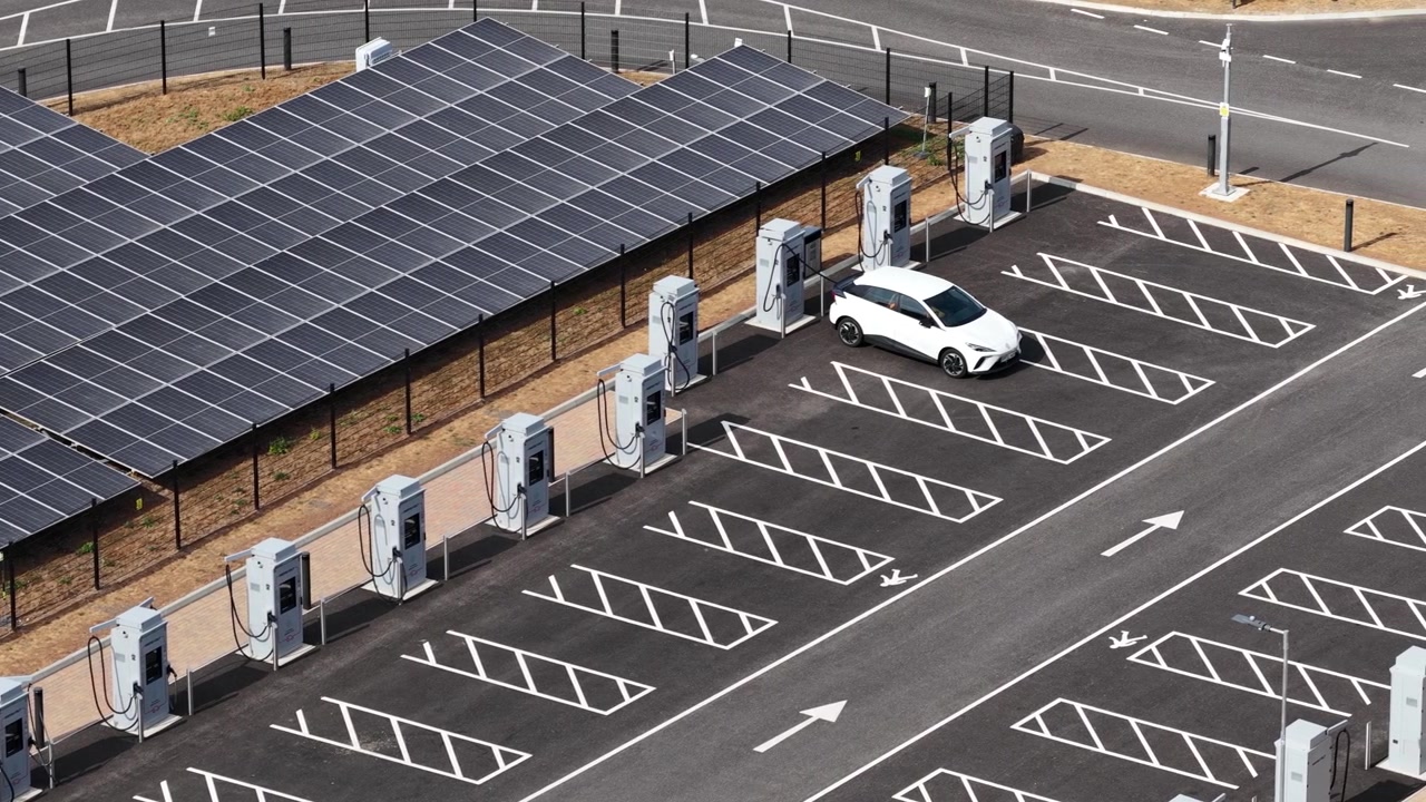 Widok z lotu ptaka nowoczesnego samochodu elektrycznego parkującego na stacji ładowania zasilanej panelami słonecznymi, prezentujący zrównoważony transport, energię odnawialną i przyszłość infrastruktury czystej mobilności