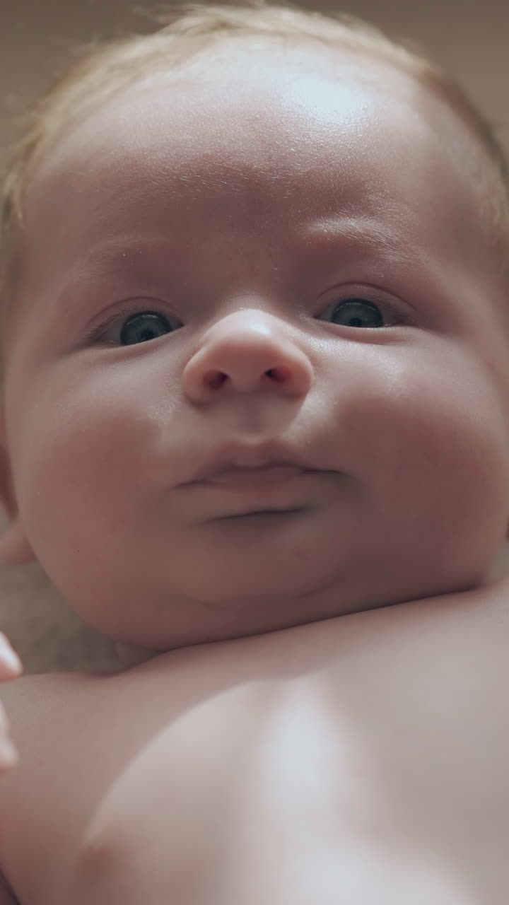 cute infant boy with short blond hair and big blue eyes lies on changing table and moves body extreme close view