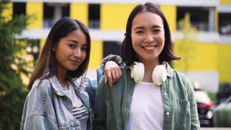 Außenporträt-Von-Zwei-Schönen-Jungen-Japanischen-Mädchen,-Die-Auf-Der-Straße-In-Die-Kamera-Lächeln-Und-Posieren-1