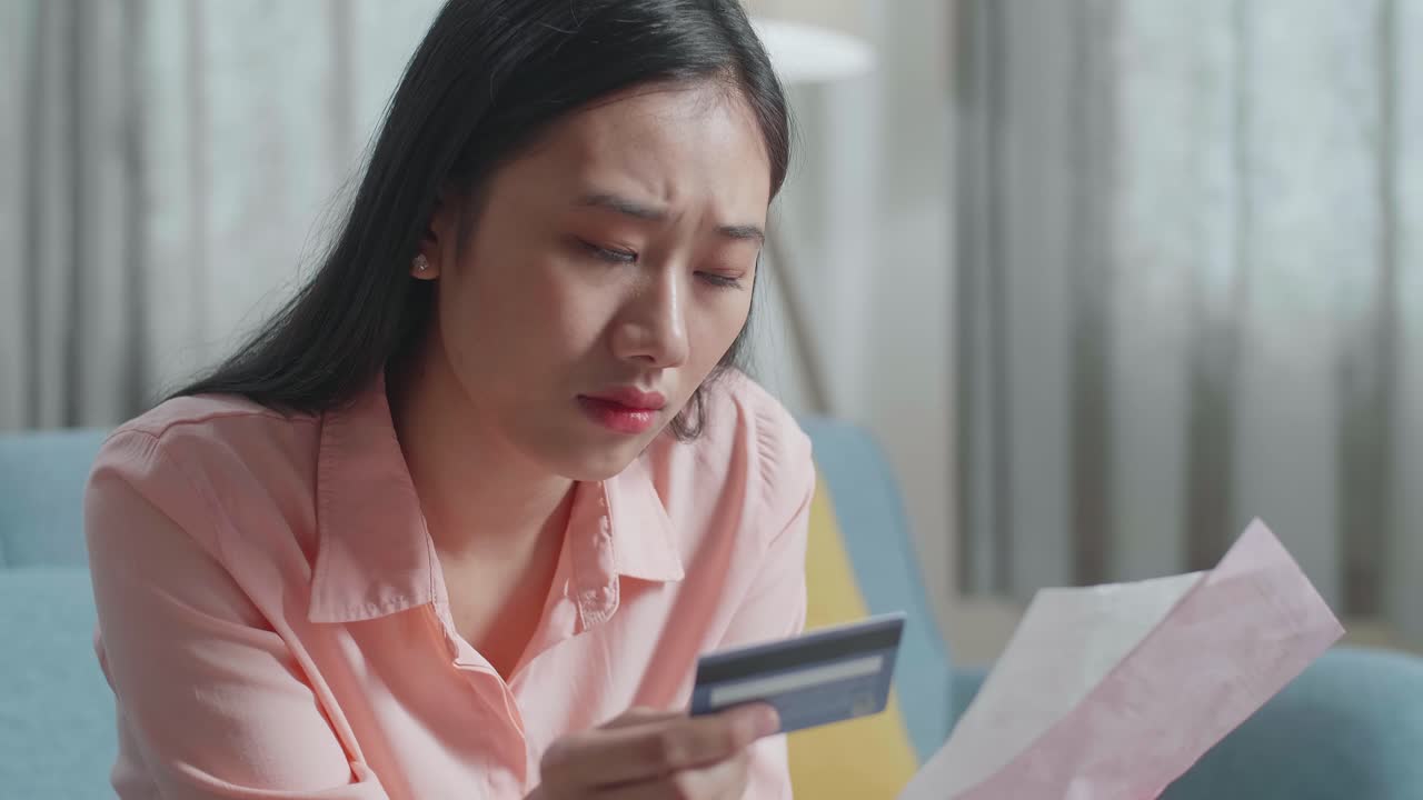 아시아 여성의 클로즈업은 청구서와 신용카드를 보고 머리를 흔들고 두통을 고 있습니다.