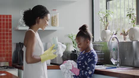 happy african american mother and daughter washing dishes in kitchen, slow motion