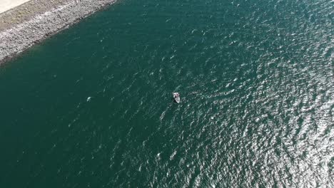 drone footage over turquiose green lake tahoe, panning down showing a small fishing boat sailing in the water and the water rippling below