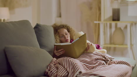 chica tendida en el sofá leyendo cuentos de hadas antes de ir a la cama