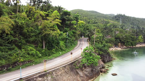 Filmische-Luftaufnahme,-Wie-Man-Mit-Einem-Motorroller-Entlang-Einer-Straße-Am-Wasser-Fährt,-Drohne,-Asien,-Cebu,-Philippinen