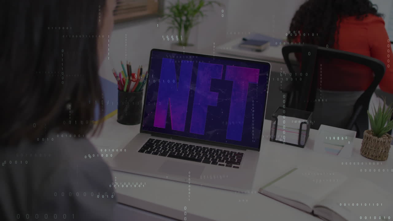 NFT text animation over person working at desk with laptop and stationery