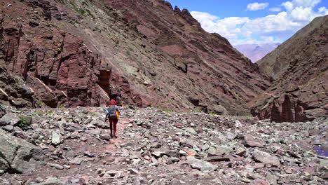 Stony-mountain-landscape-as-a-single-man-walking-through-on-a-dust-road-with-backpack