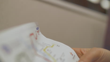 close up view of hand with paper map of subway station and then reflection of map in train window