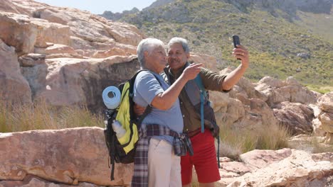 Happy-senior-biracial-couple-in-mountains-taking-selfie-with-smartphone,-in-slow-motion