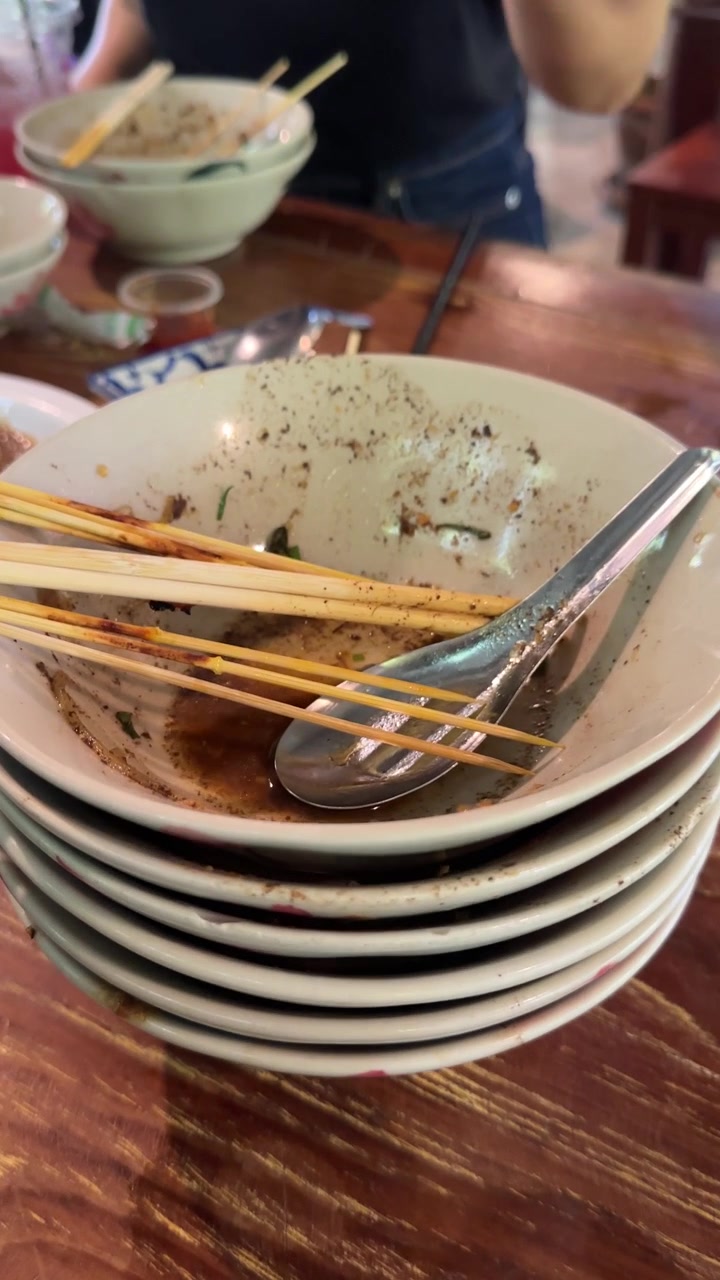 A person stacks an empty ceramic noodle bowl onto a tall pile at a restaurant.
