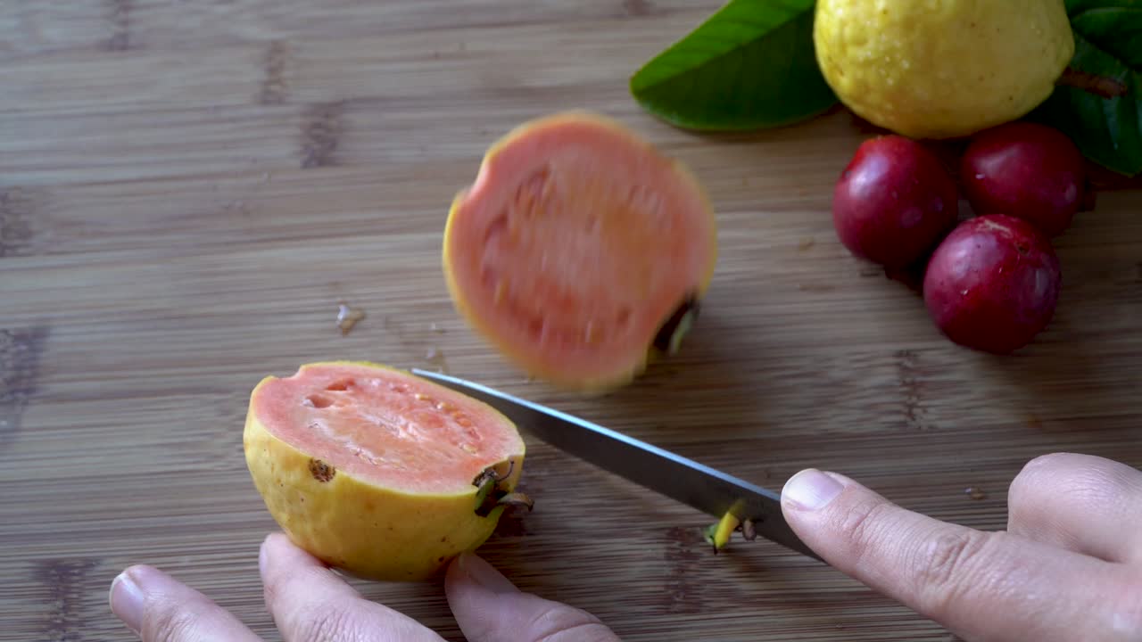 las manos cortan la fruta de guayaba de manzana amarilla madura con un cuchillo que revela el interior rosa