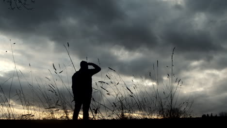 hiker looks over field at golden hour with dramatic clouds overhead