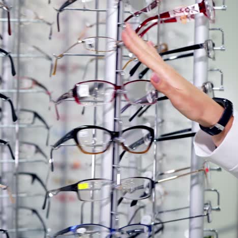young female choosing eyeglasses in the store. hands of a woman customer spinning the stand with fashionable spectacles at optics.