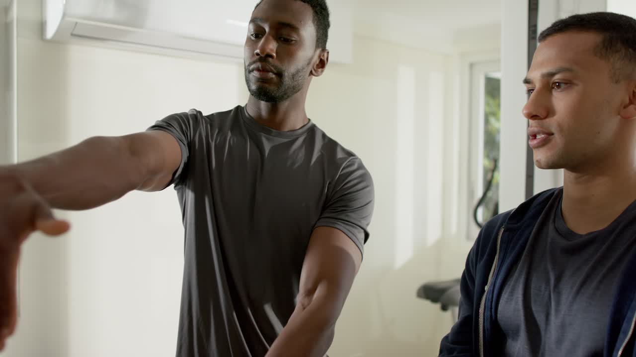 Male trainer demonstrating wrist stretch in gym, male client mirroring for mobility warmup