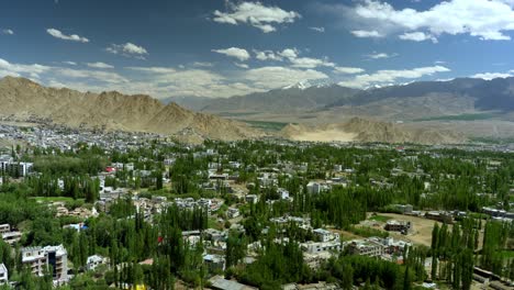 vibrant leh city surrounded with green trees and himalayan mountains under clear blue sky, leh palace in view at distance, ladakh, kashmir, timelapse