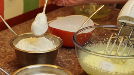 hand adding flour with spoon to mixed egg yolk, preparation of sponge cake, closeup