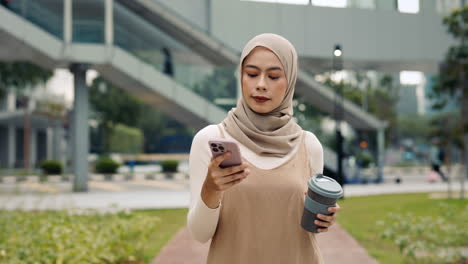 Woman in hijab using mobile phone and holding a cup