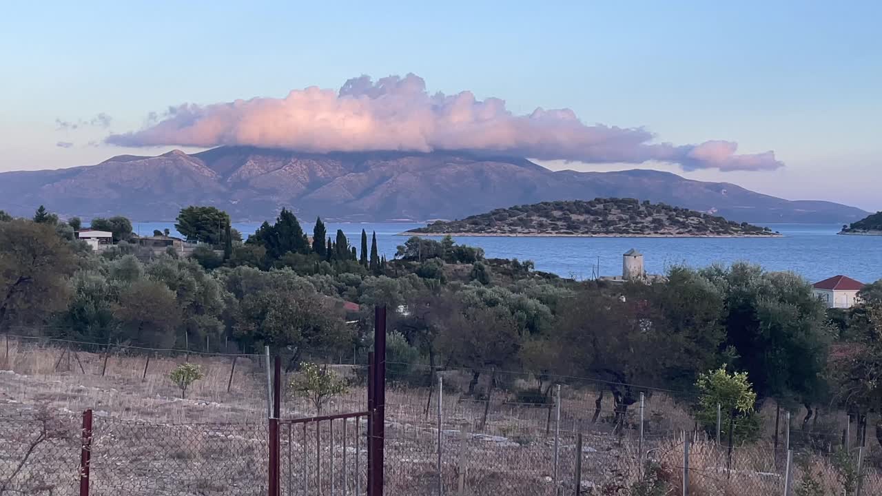 Kalamos Island and Mytikas,Still Frame,Footage from a country side towards the mountains covered with white pink clouds at mainland. Beautiful country side with olive trees,windmill