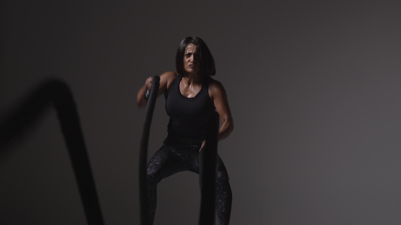 Studio Shot Of Mature Woman Wearing Gym Fitness Clothing Doing Cardio Exercise With Battle Ropes 3