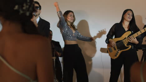 clip of an elegant party where women in formal dresses enjoy live music. a band can be seen livening up the event.