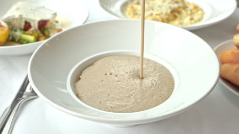 verter sopa de crema de champiñones en un tazón blanco servido como parte de un curso de almuerzo en un restaurante italiano
