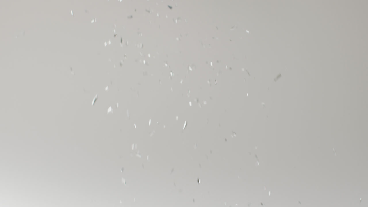 Video of glittering silver confetti falling on white background