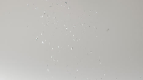 video of glittering silver confetti falling on white background