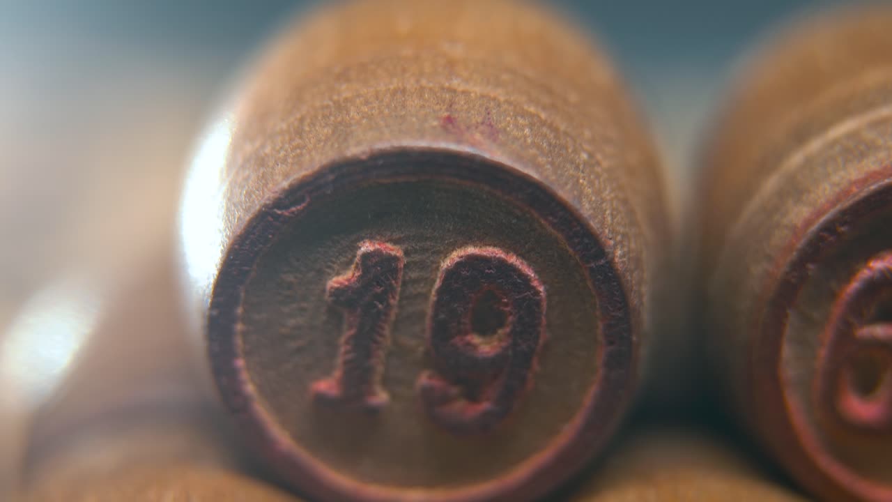 macro cinematográfico plano suave de barriles de madera de bingo en una fila, figuras de madera, números antiguos juego de mesa vintage, número de la suerte 19, cámara lenta, movimiento de gimbal comercial de 4k, iluminación de ensueño, inclinación hacia arriba