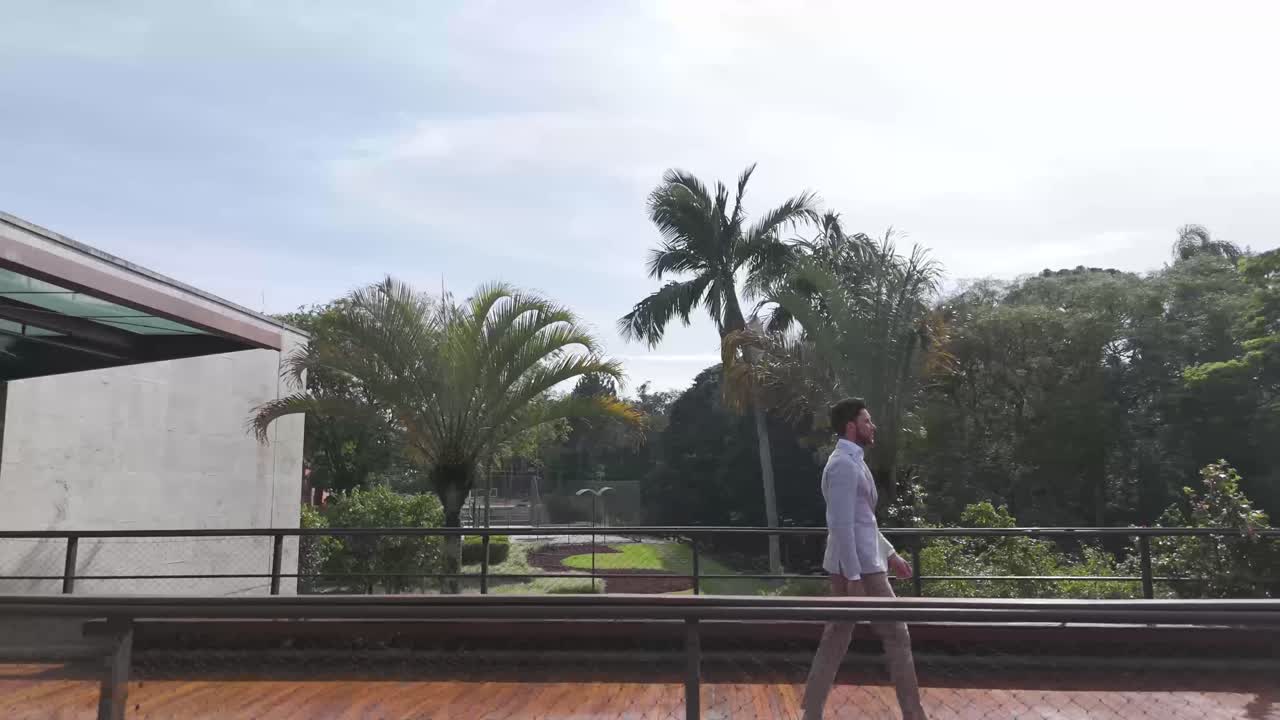 Man in Elegant Suit Walking on Bridge with Tropical Greenery in the Background
