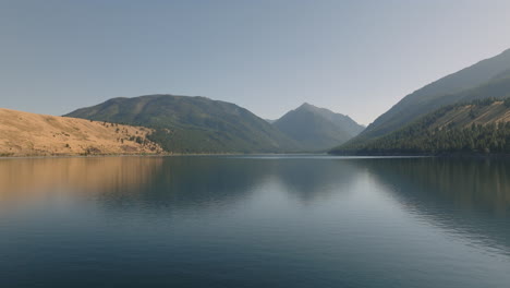 Scenic-aerial-moving-across-mountain-lake-with-reflection