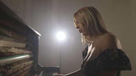 woman playing upright piano with open sound board showing hammers striking the strings-1