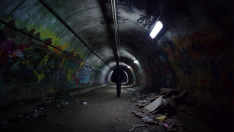 person walking through graffiti-covered abandoned tunnel