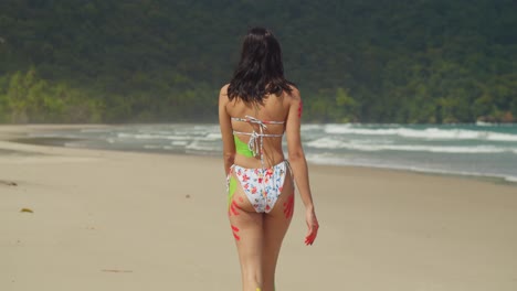 enjoying the warmth of the caribbean sun, a girl in a bikini and body paint walking on a white sand beach